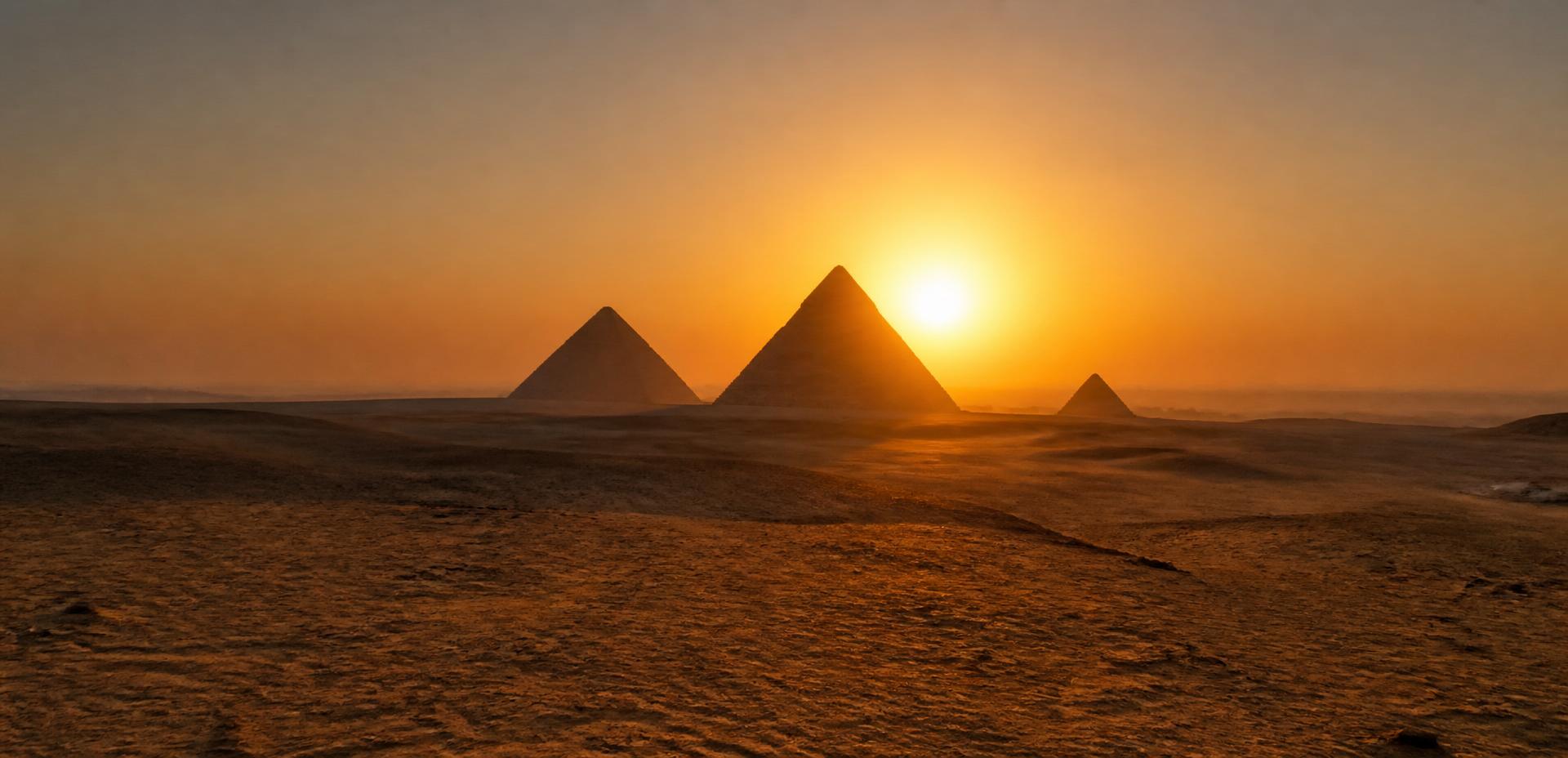 The Pyramids of Giza silhouetted against the setting sun over the desert plateau
