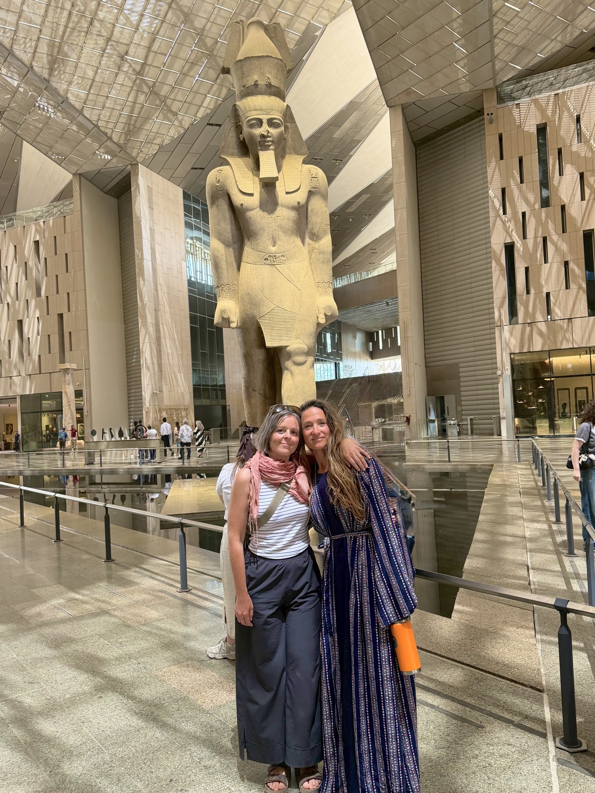 Two friends together beneath the colossal statue of Ramses II at the Grand Egyptian Museum
