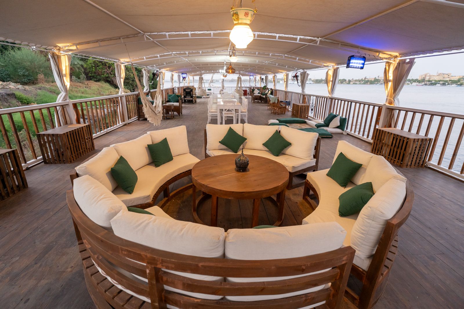 Curved sofa lounge on the dahabiya's shaded upper deck at dusk on the Nile